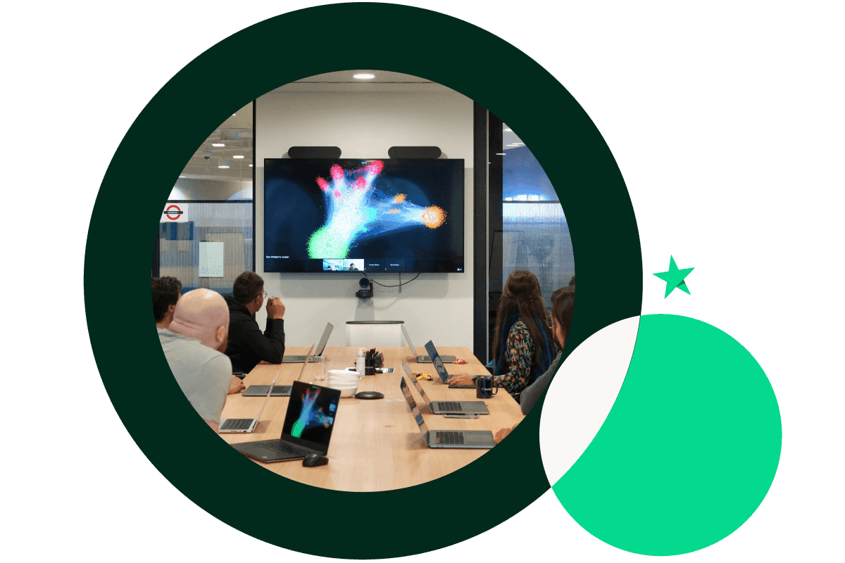 A graphic of a large dark Green circle and a smaller bright Green circle. The large circle features an image of a group of a people looking at a screen in a meeting room. The smaller circle features the Trustpilot star above it.